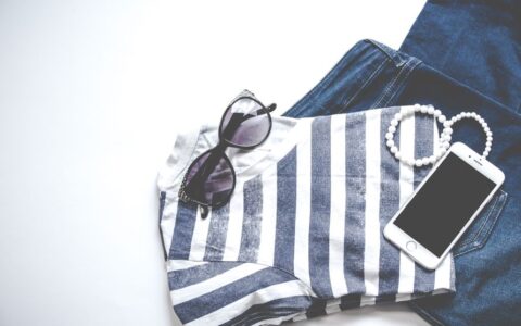Flat lay image featuring sunglasses, striped top, jeans, and smartphone, ideal for fashion and lifestyle themes.