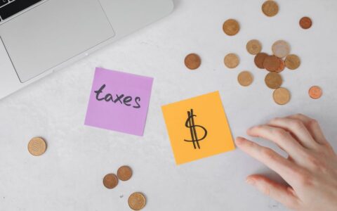 Overhead view of coins, sticky notes with tax symbols, and a hand on a desk.