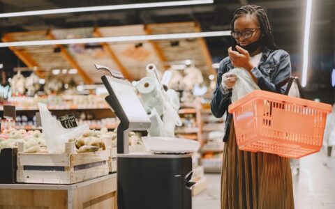A woman shopping in a supermarket, checking items with a basket in hand.