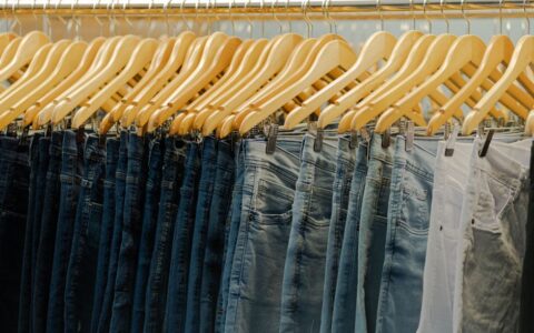 Close-up of various denim jeans hanging on wooden hangers in a fashionable store.