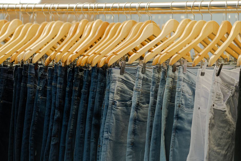 Close-up of various denim jeans hanging on wooden hangers in a fashionable store.