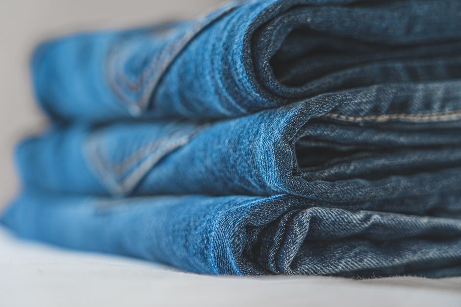 Detailed close-up image of a neat stack of blue folded denim jeans highlighting the fabric texture.
