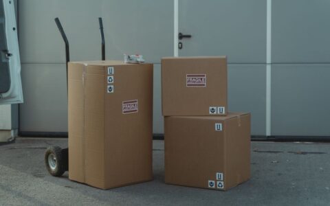 Three cardboard boxes on a dolly, ready for shipping outside a warehouse.