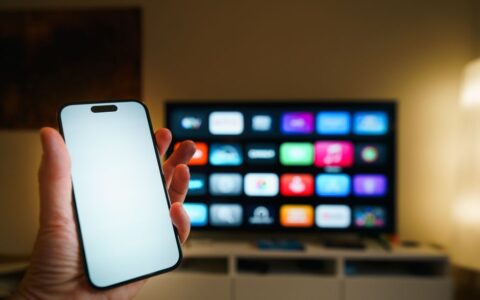 A smartphone in focus with a smart TV displaying apps in a cozy living room.
