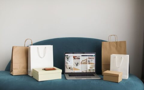 A laptop surrounded by shopping bags and boxes on a blue sofa, ideal for online shopping themes.