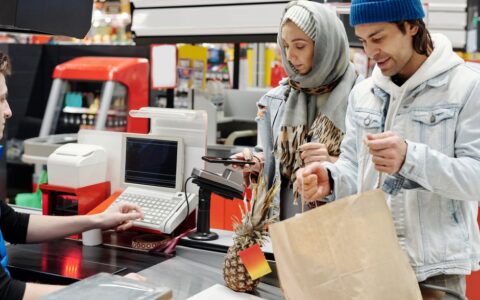 A Middle Eastern couple making a purchase at a supermarket checkout using a smartphone.