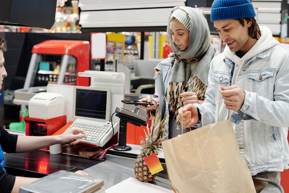 A Middle Eastern couple making a purchase at a supermarket checkout using a smartphone.