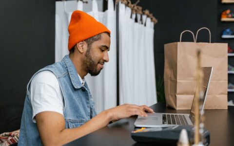 Man in a beanie using laptop in a stylish fashion store, indoors.
