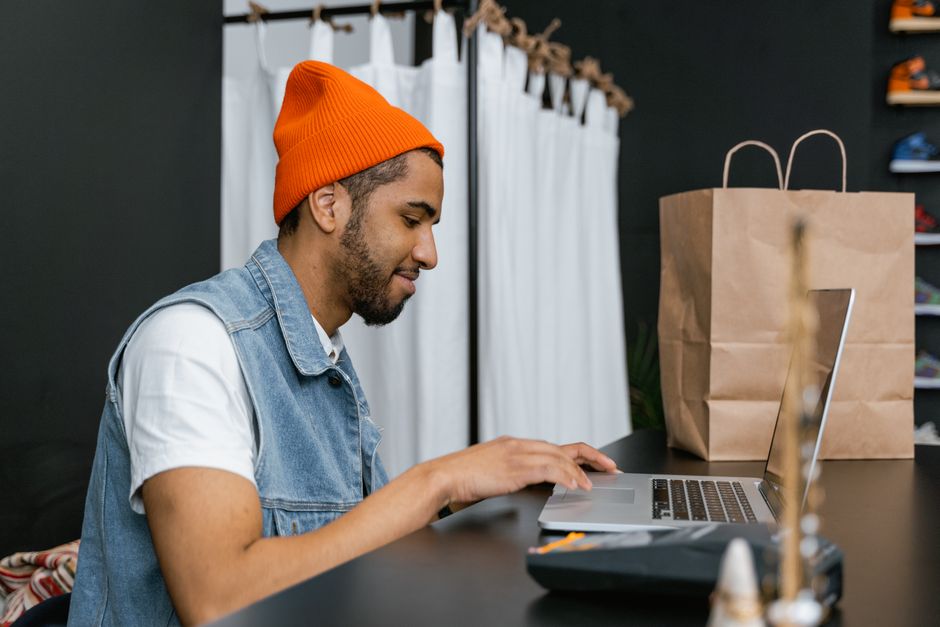 Man in a beanie using laptop in a stylish fashion store, indoors.