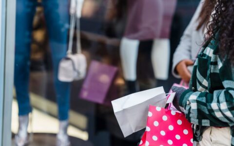 Crop anonymous women friends in stylish clothes standing with shopping bags near counter of boutique in daytime