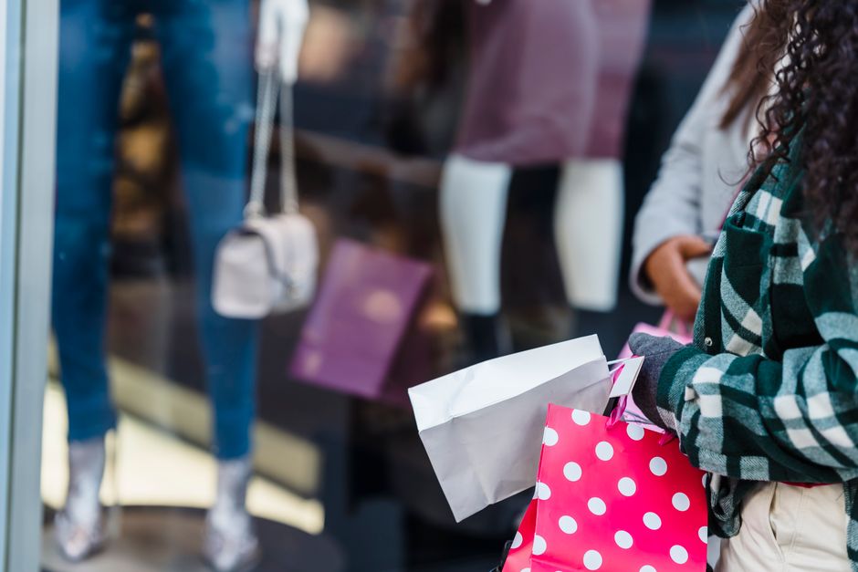 Crop anonymous women friends in stylish clothes standing with shopping bags near counter of boutique in daytime