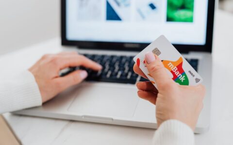 Close-up of hands using a laptop and holding a credit card for an online transaction.
